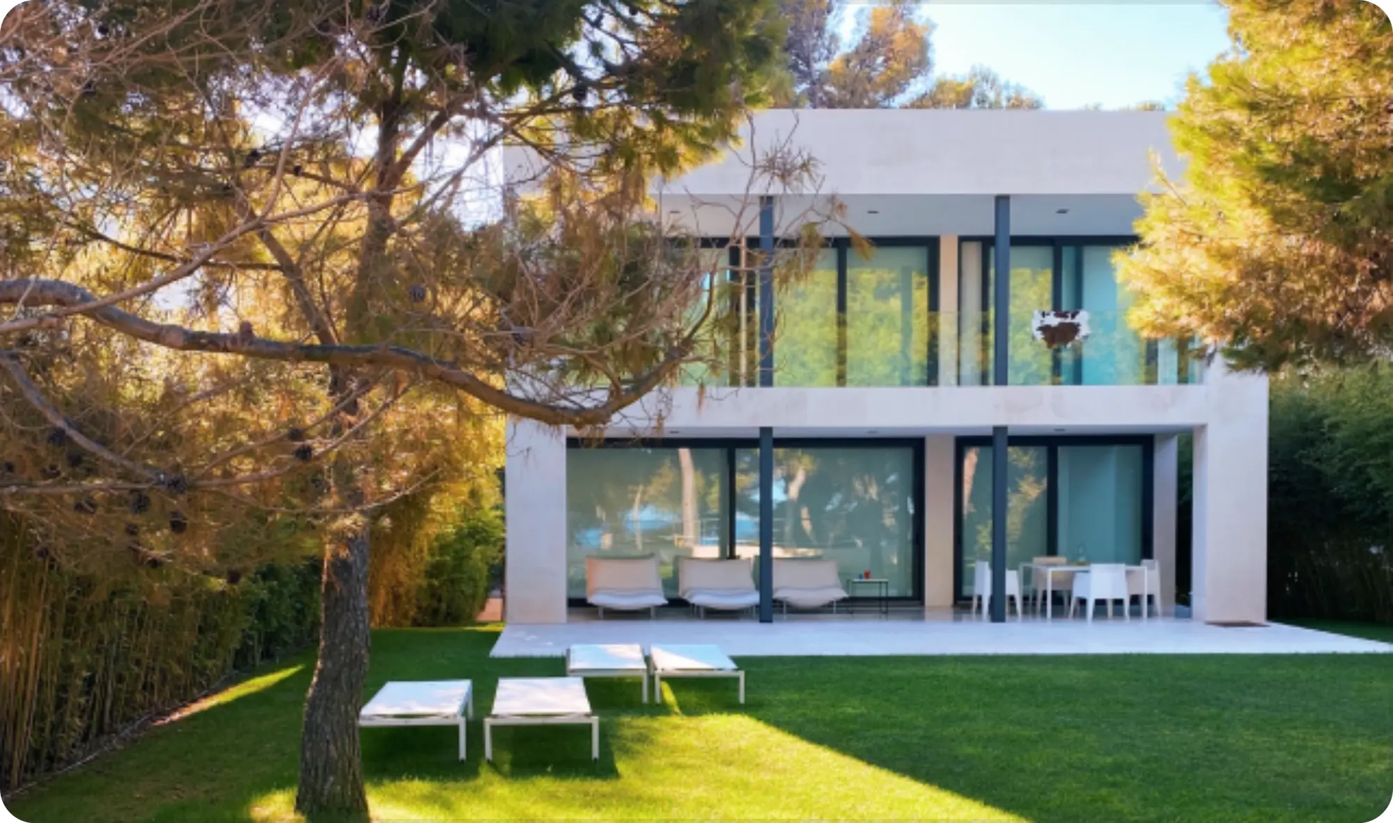 Modernes Einfamilienhaus mit großen Glasfronten und Sonnenliegen im Garten im sonnigen Herbst